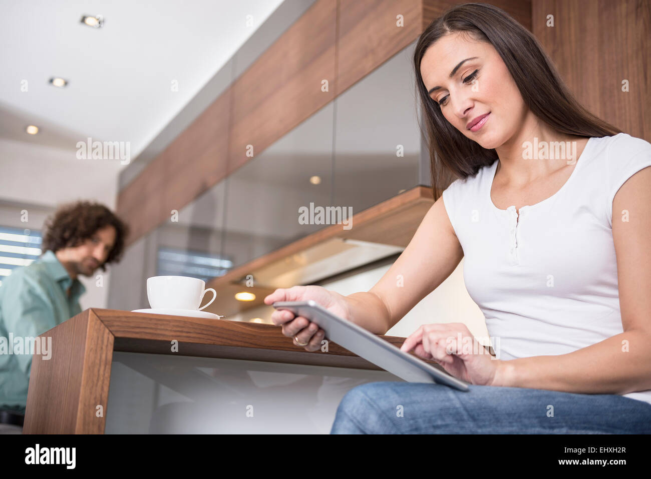 Donna che utilizza una tavoletta digitale mentre suo marito una cottura in cucina, Monaco di Baviera, Germania Foto Stock