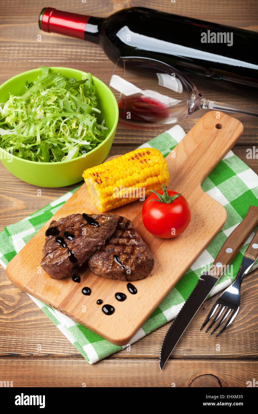 Bistecca alla griglia con mais, insalata e vino rosso su un tavolo di legno Foto Stock