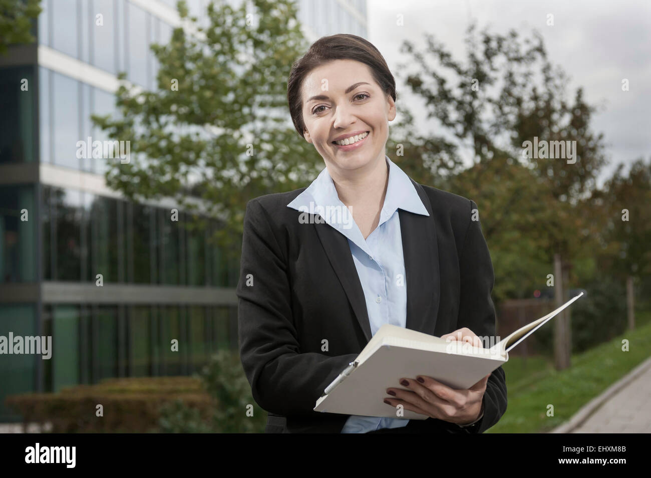Donna d'affari che scrive appunti all'organizzatore personale di fronte a un edificio per uffici, Baviera, Germania Foto Stock
