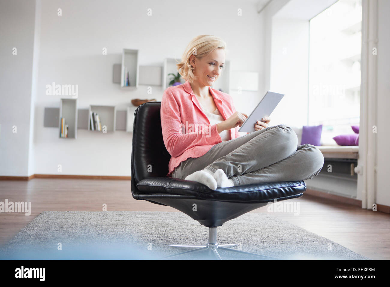Donna rilassante con tavoletta digitale sulla sedia in pelle a casa Foto Stock