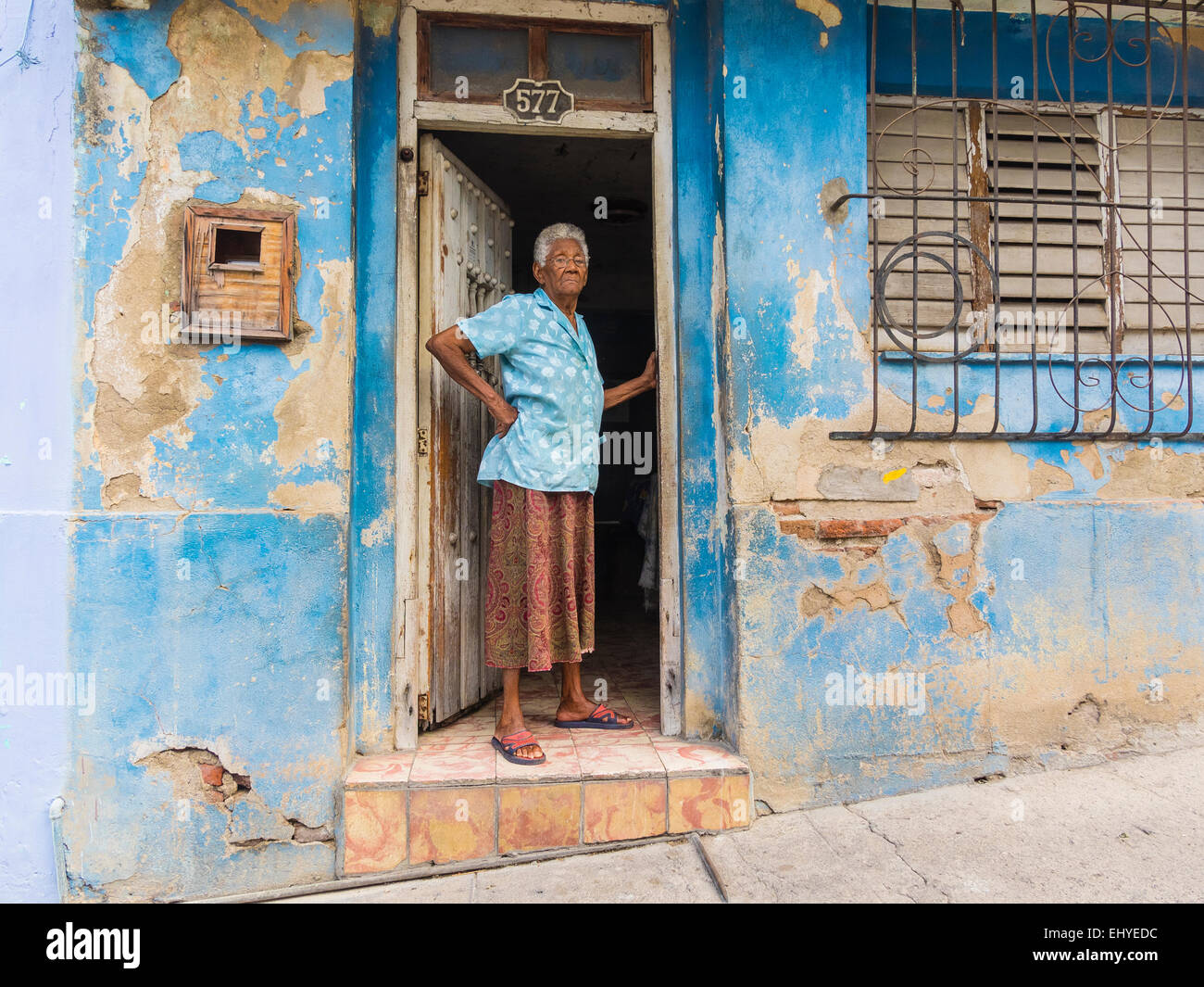 Senior afro-cubane nella porta di crumbing parete blu in Santiago de Cuba. Foto Stock