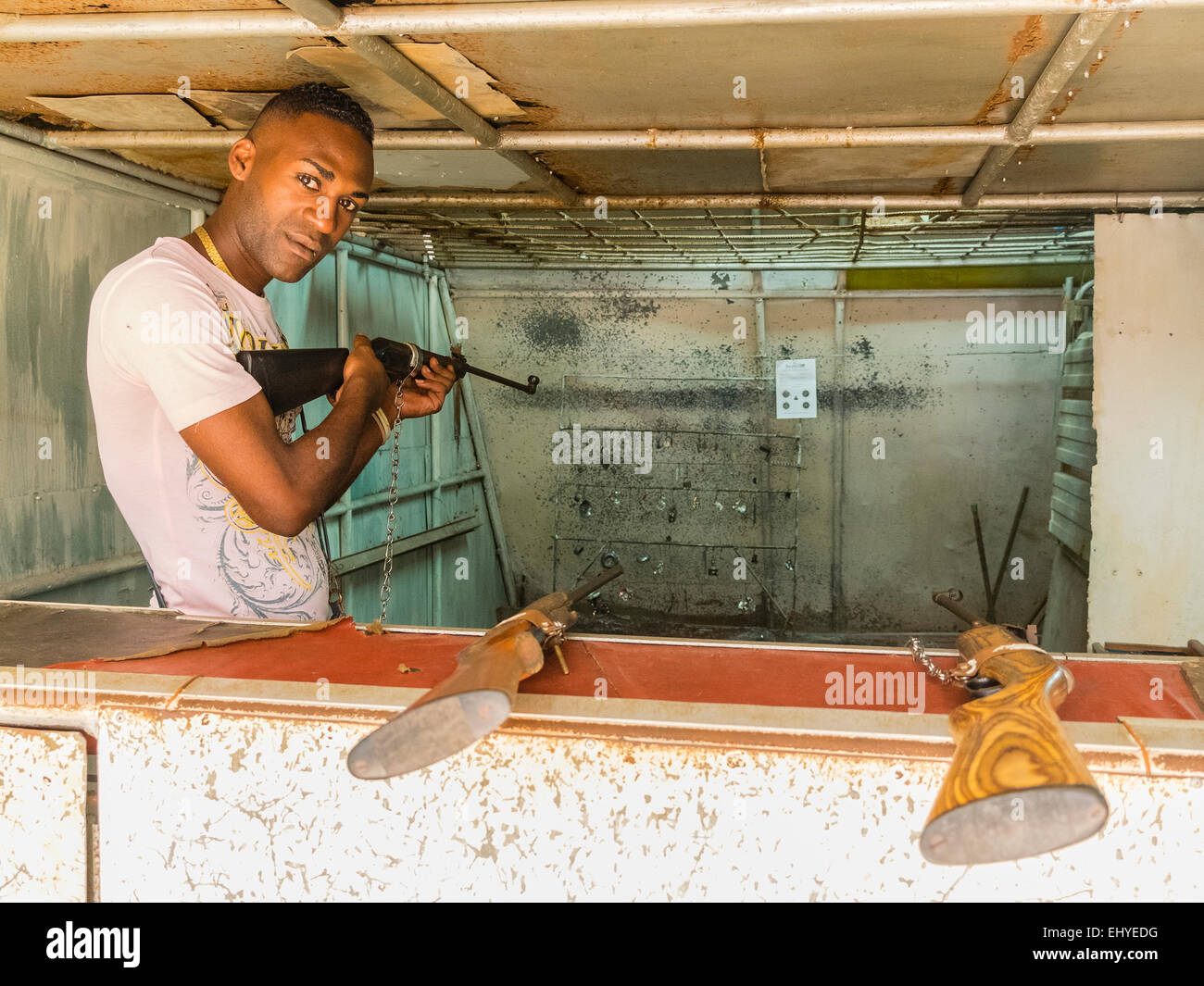Un uomo afro-cubane detiene un fucile presso la galleria di tiro che gestisce. Foto Stock