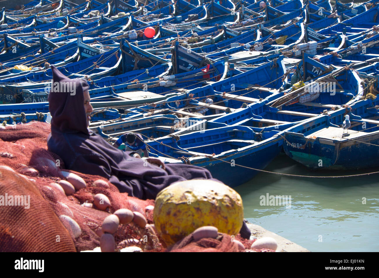 Barche da pesca e uomo in abito tradizionale nel porto di Essaouira, Marocco, Africa del Nord Foto Stock