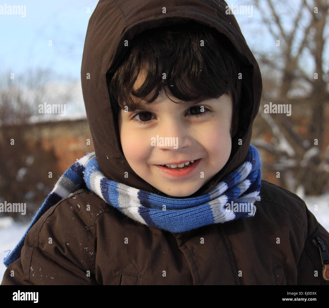 Ragazzo di età prescolare con auburn i capelli e gli occhi castani sta giocando con la neve fuori in un giorno d'inverno. Egli è vestito con il caldo panno invernale Foto Stock