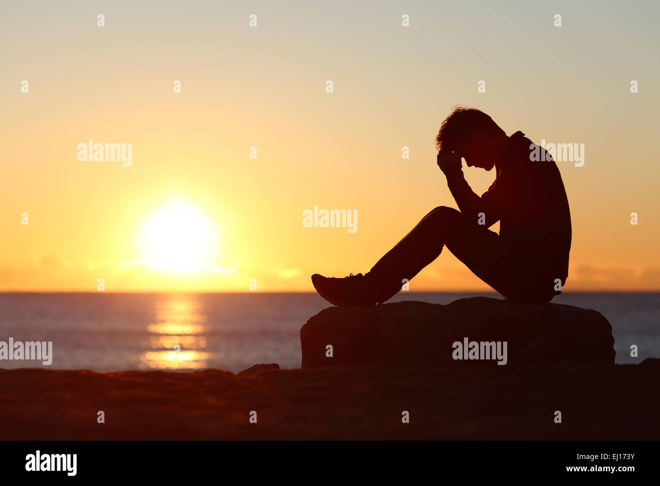 Triste silhouette uomo preoccupato sulla spiaggia al tramonto con il sole in background Foto Stock