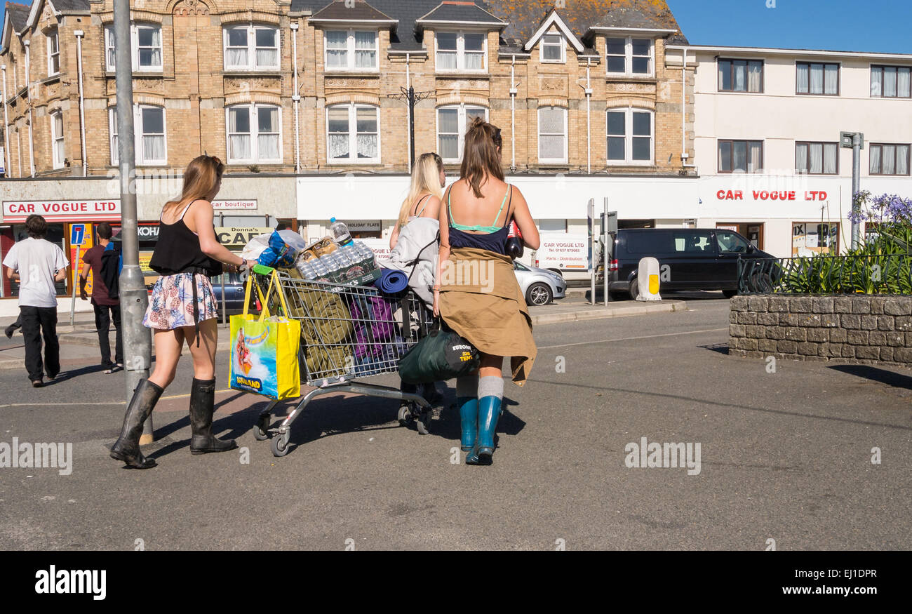 3 ragazze spingere i loro averi in un carrello della spesa sul loro modo al Festival Boardmasters in Newquay Foto Stock