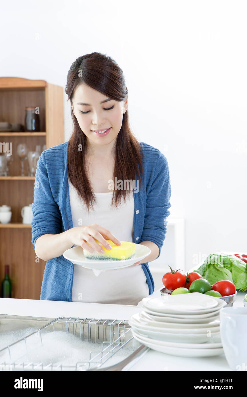 Giovane donna piastre di lavaggio nel lavello da cucina con sorriso, Foto Stock