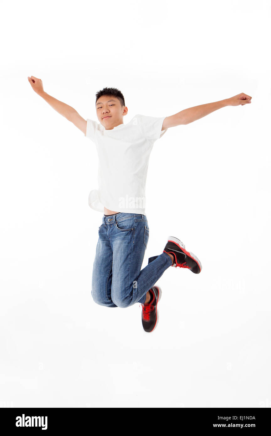 Ragazzo adolescente jumping in mid-aria con le braccia aperte Foto Stock