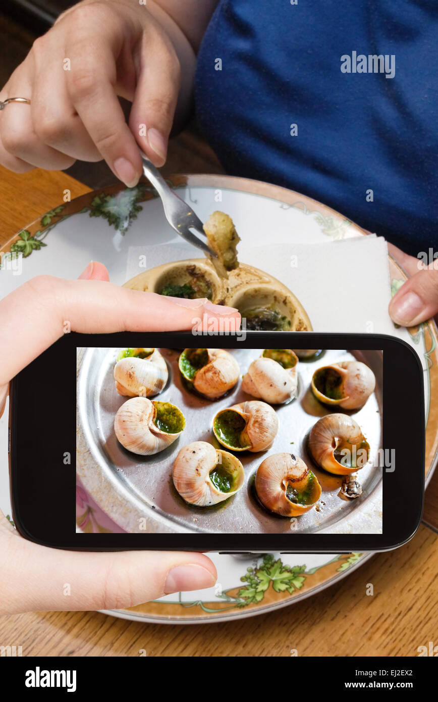 Fotografare il concetto di cibo - tourist prende immagine della piastra calda di escargot conchiglie, con apposite pinze e la forcella sullo smartphone, Foto Stock