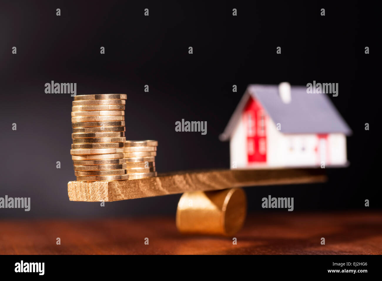 Altalena con una casa su di un lato e pile di monete sull'altro lato. Foto Stock