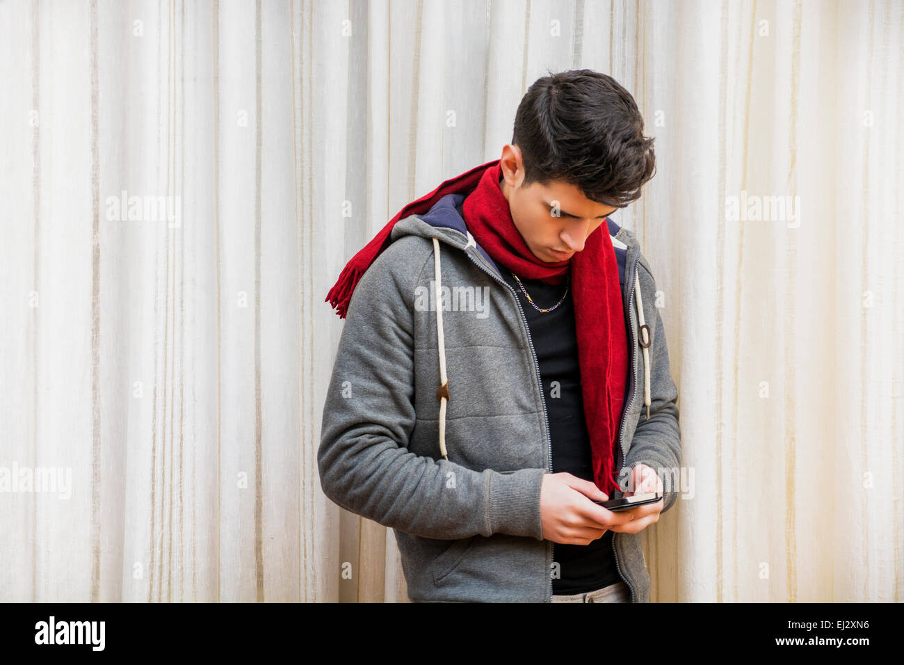 Giovane uomo in piedi indoor la digitazione di un messaggio di testo sul suo telefono con le sue dita come egli comunica con gli amici Foto Stock
