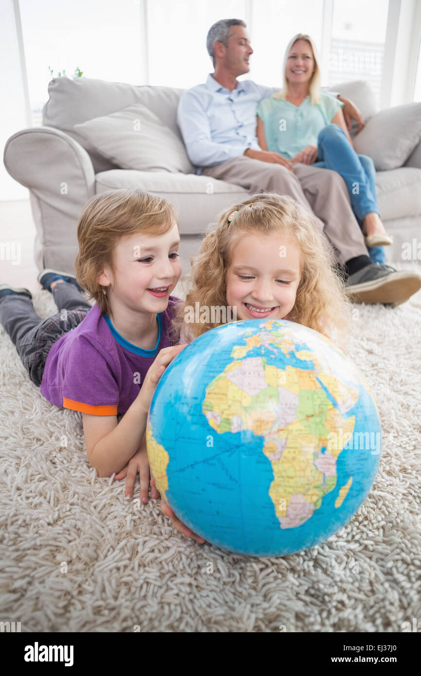 I bambini ad esplorare globe mentre i genitori seduti sul divano Foto Stock