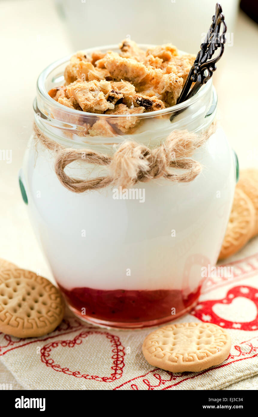 Luce di yogurt con frumento integrale biscotti sbriciolati e marmellata di frutti di bosco nel cuore decorate panno. DOF poco profondo, il fuoco selettivo Foto Stock