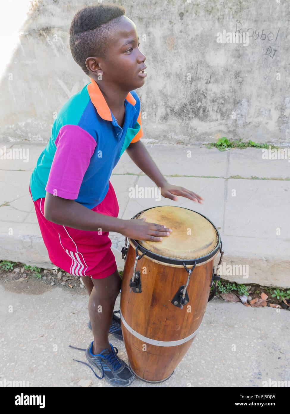 Vista laterale di un 10-12 anni ragazzo afro-cubane giocando conga tamburo nelle strade di l'avana al di fuori della sua casa.. Foto Stock