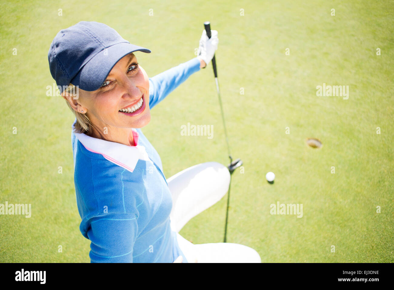 Signora sorridente golfista inginocchiato sul putting green Foto Stock