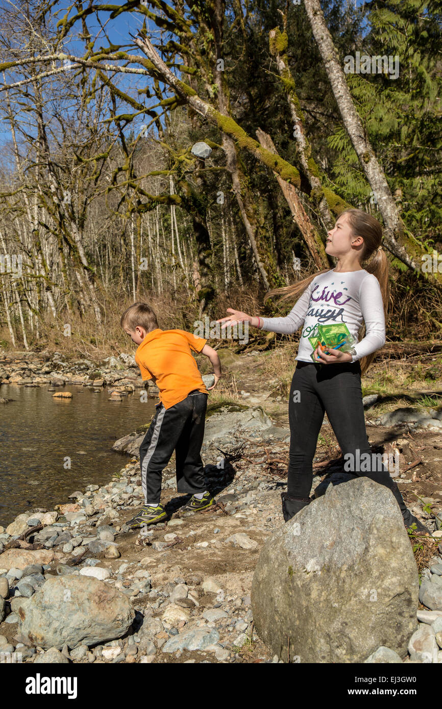 9 anno vecchia ragazza lanciando una roccia in aria e dei suoi sette anni di vecchio ragazzo gettando una roccia nel fiume Snoqualmie Foto Stock