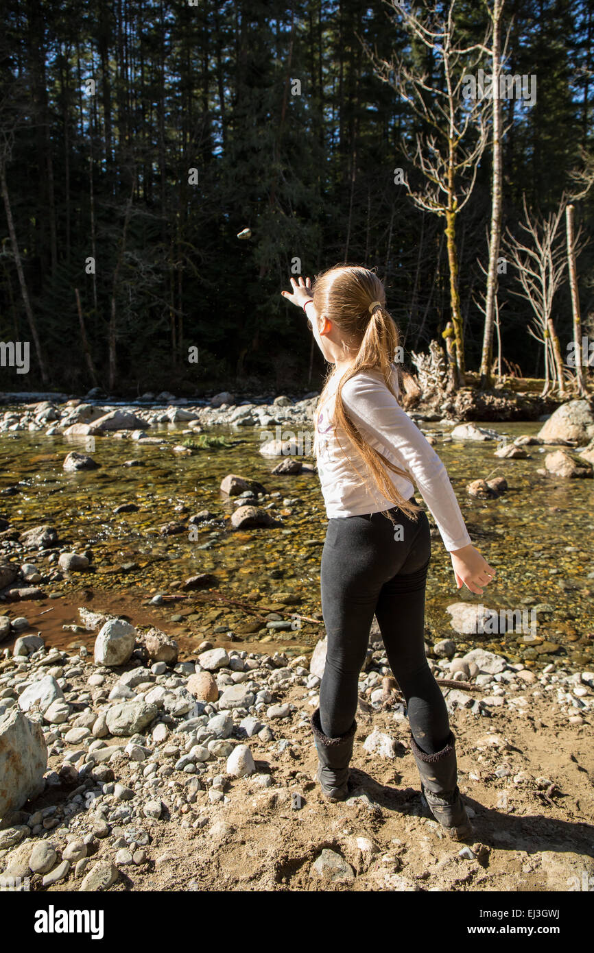 9 anno vecchia ragazza gettando una roccia (con la roccia in aria) nel fiume Snoqualmie, vicino a North Bend, Washington, Stati Uniti d'America Foto Stock