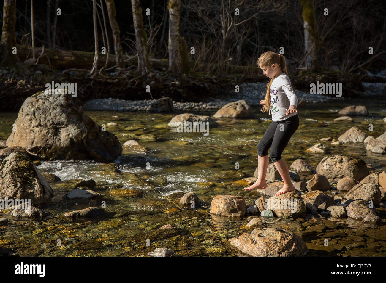 9 anno vecchia ragazza bilanciamento come lei si arrampica sulle rocce in poco profondo fiume Snoqualmie, vicino a North Bend, Washington, Stati Uniti d'America Foto Stock