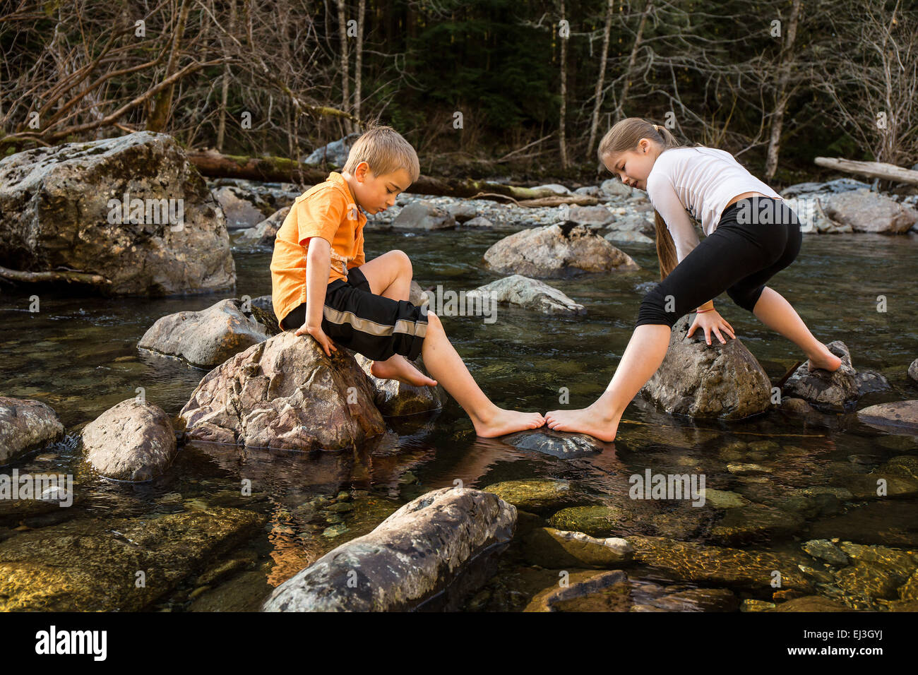 Impasse di un 9 anno vecchia ragazza che vogliono andare nella direzione opposta a quella del suo 7 anno vecchio fratello come la roccia hop nel fiume Foto Stock