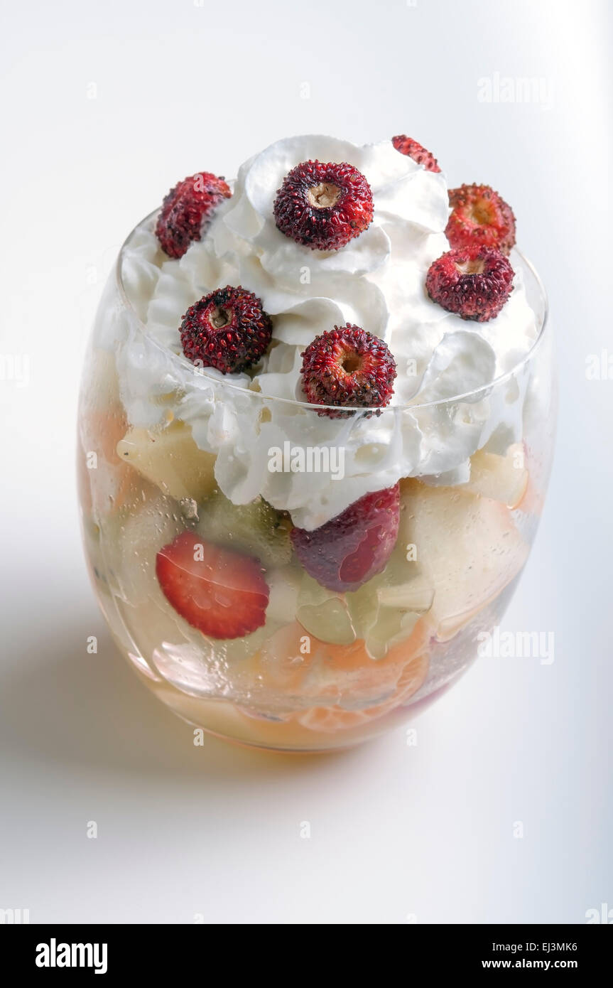 Insalata di frutta con un bicchiere di panna e fragole su sfondo bianco Foto Stock