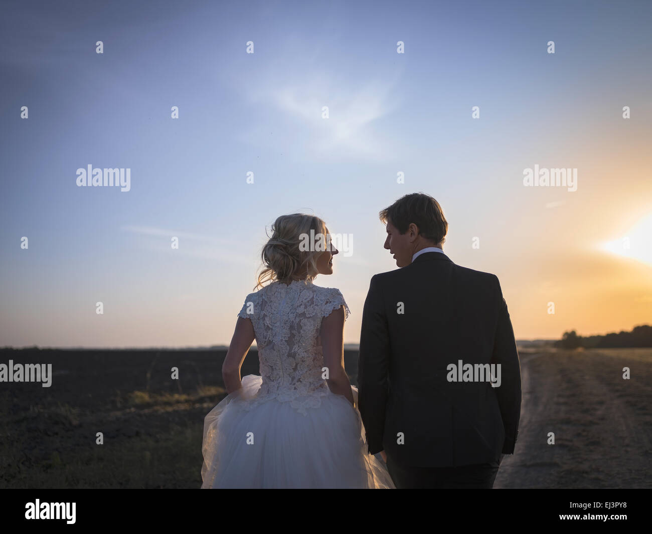 Giovani coppie in viaggio di nozze a parlare sul campo al tramonto. Sposi b Foto Stock