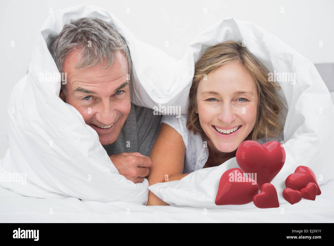 Immagine composita di felice coppia di mezza età sotto il piumino Foto Stock