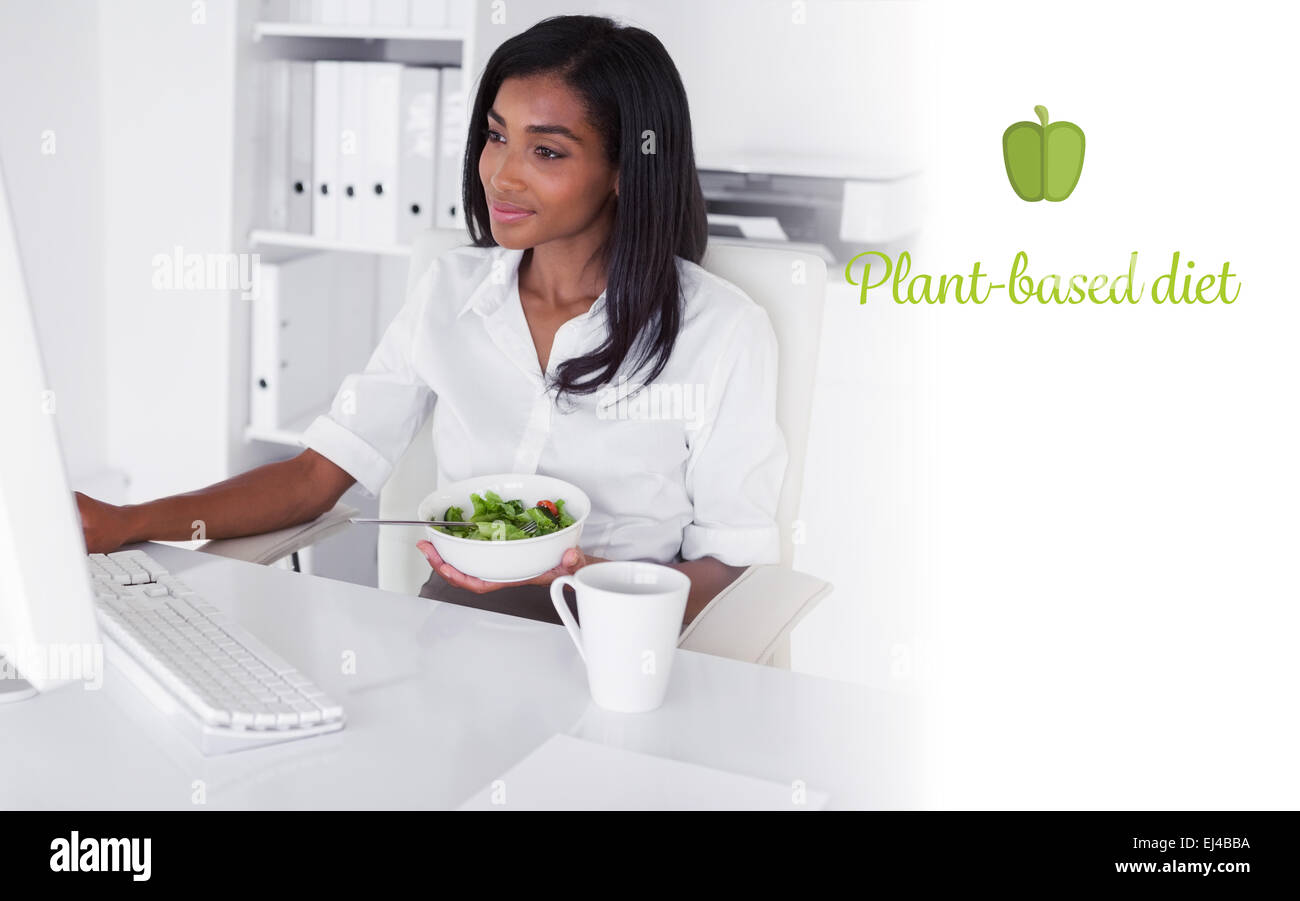 Dieta a base di piante contro felice piuttosto imprenditrice di mangiare un insalata alla sua scrivania Foto Stock