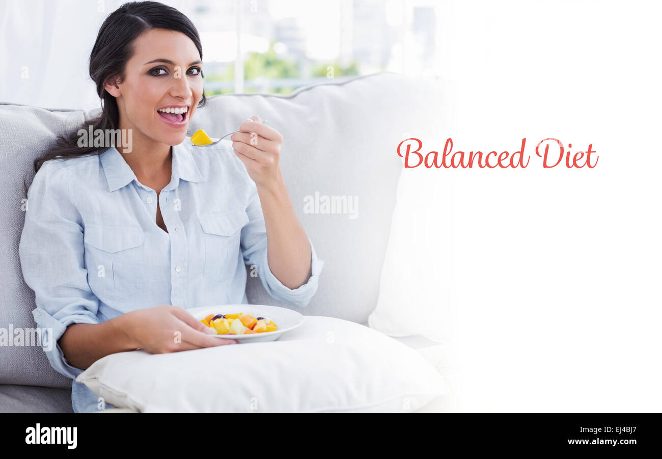 Dieta equilibrata contro la donna felice seduta sul divano a mangiare insalata di frutta Foto Stock