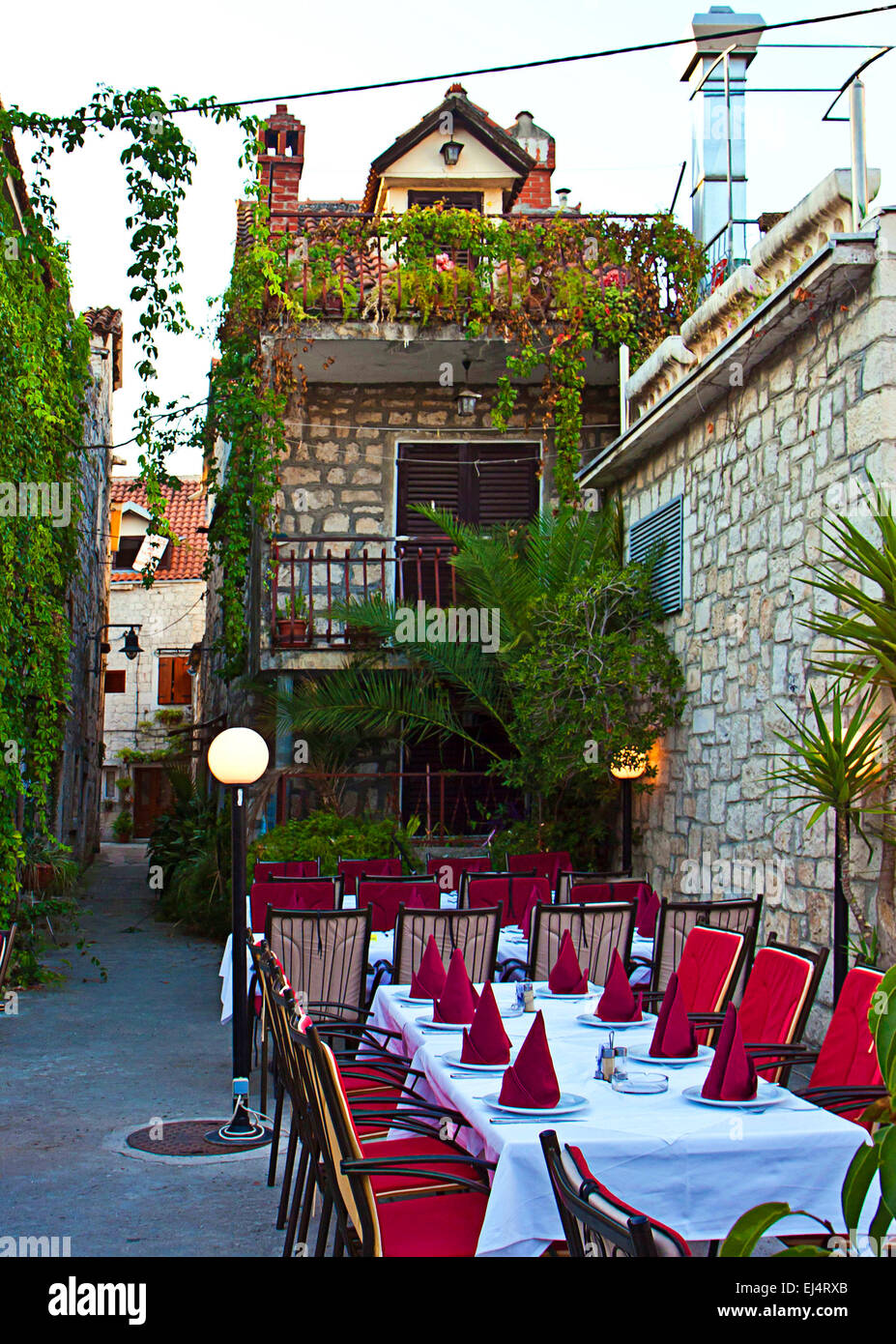 Il Trogir Croazia, è tarda sera, le lampade sono accese e un ristorante con posti a sedere e tavoli sulla strada è pronto per i turisti Foto Stock