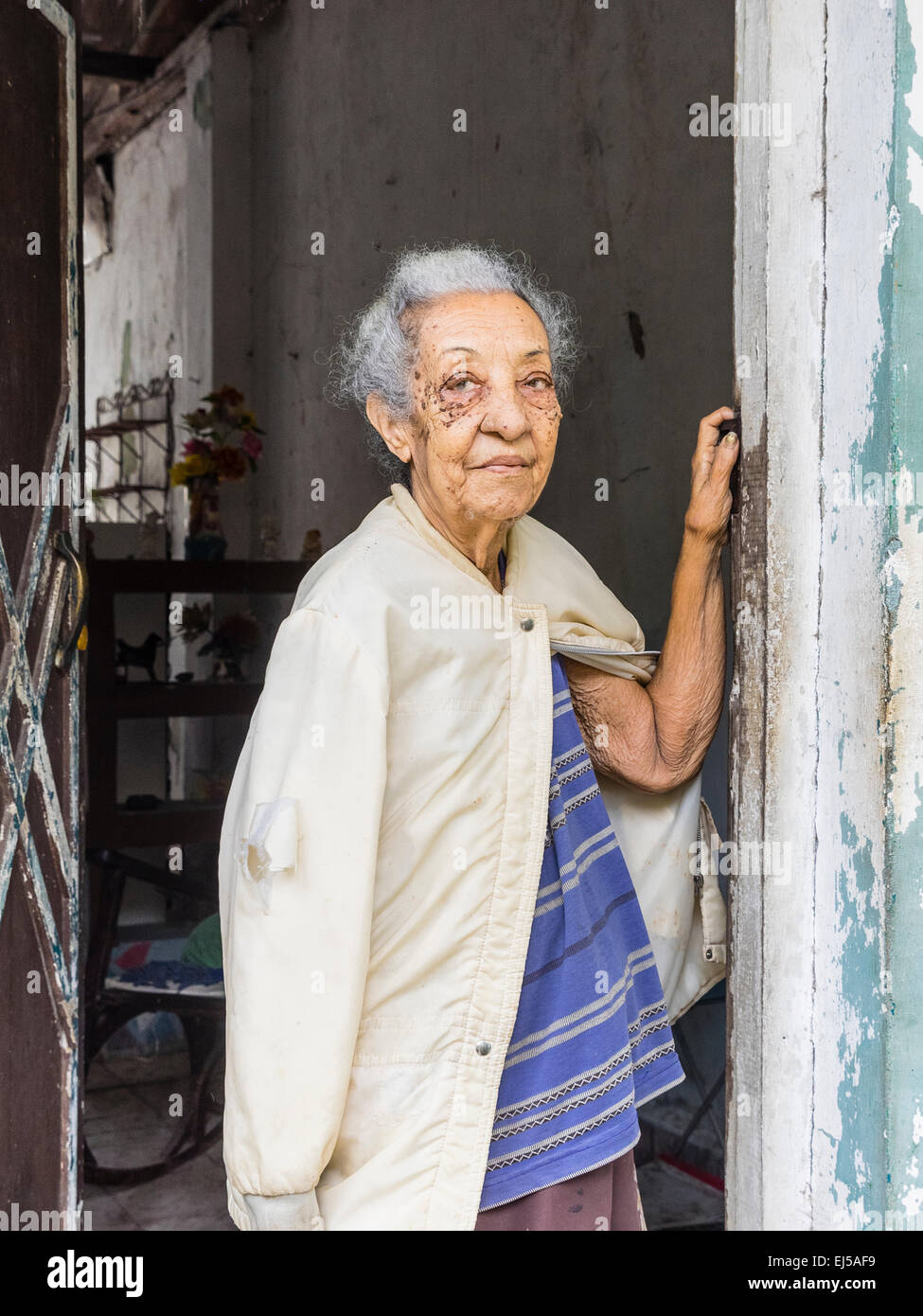 Femmina afro-cubane senior citizen con i capelli grigi si erge sulla porta della sua casa guardando fuori con un braccio contro la porta. Foto Stock