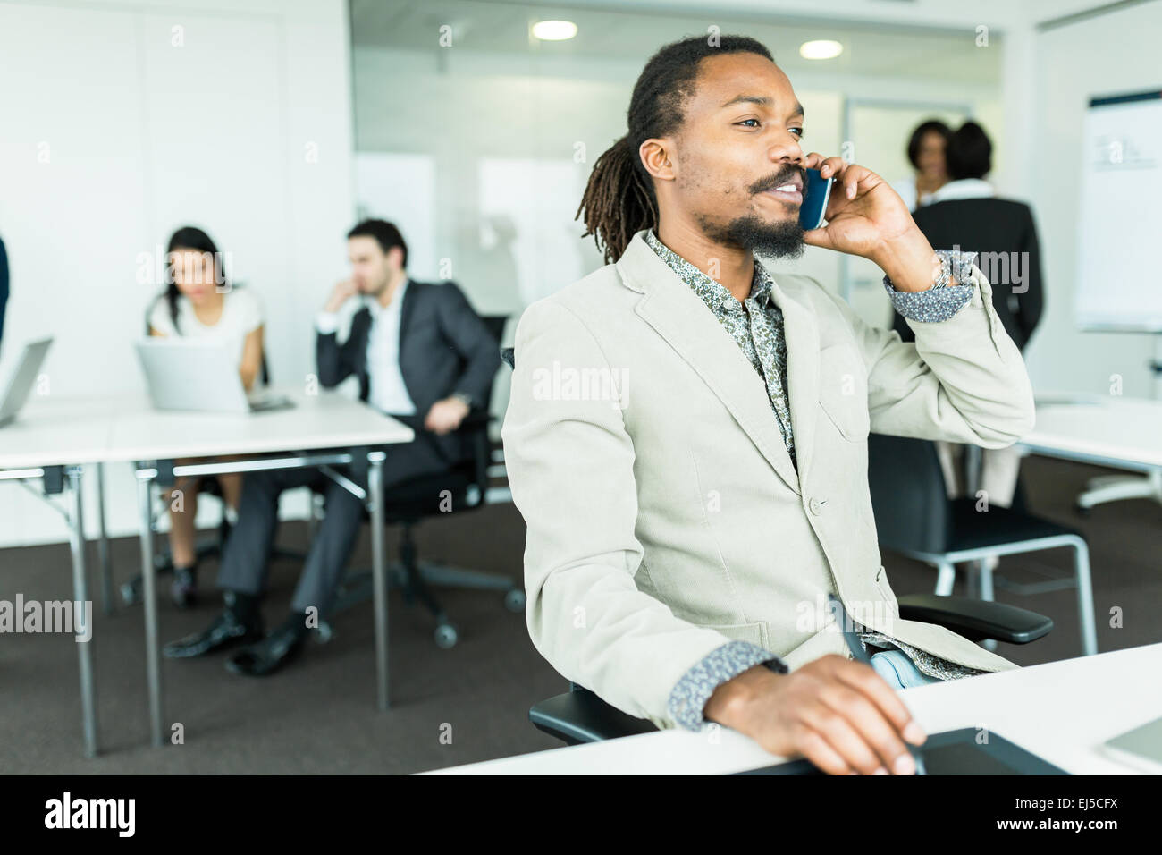 Nero bello graphics designer con dreadlocks mediante digitalizzatore in una ben illuminata, ordinato ufficio ambiente e parlando al telefono Foto Stock