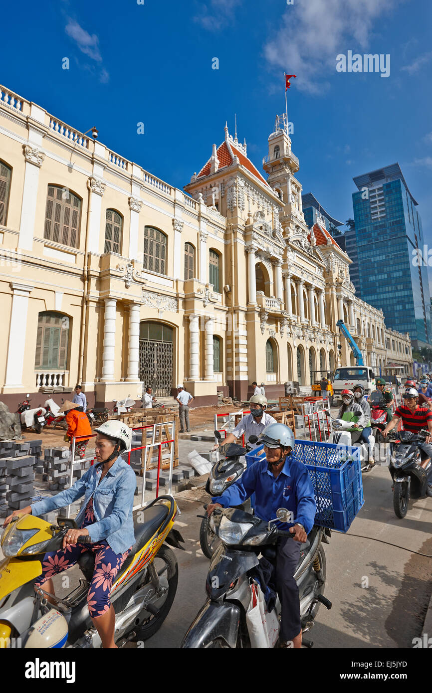 La popolazione locale sulla moto in movimento nella parte anteriore del popolo del comitato dell edificio. La città di Ho Chi Minh, Vietnam. Foto Stock