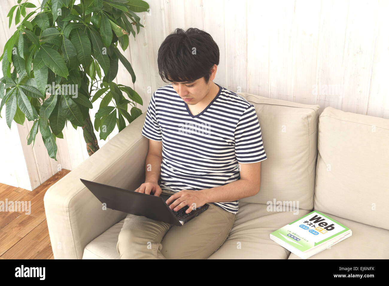 Un giovane giapponese uomo che lavora presso il suo computer portatile sul divano Foto Stock