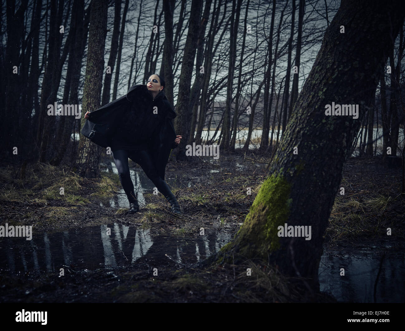 Moda donna che indossa un cappotto invernale e si pongono in una cupa foresta, freddo pioggia, Croce trasformati a piena lunghezza immagine Foto Stock