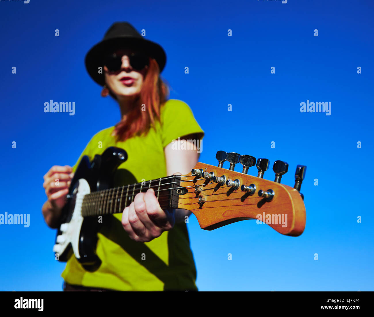 Suonatore ambulante femmina con la chitarra elegante musicista femmina con i capelli rossi indossatore in black hat e camicia verde gioca sulla chitarra. Foto Stock