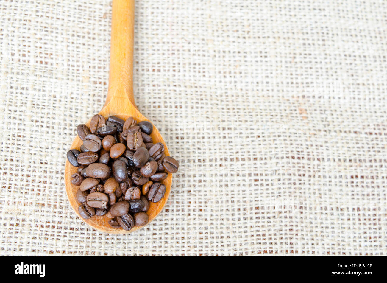 Cucchiaio di legno pieno con chicchi di caffè tostati su una tovaglia vintage Foto Stock