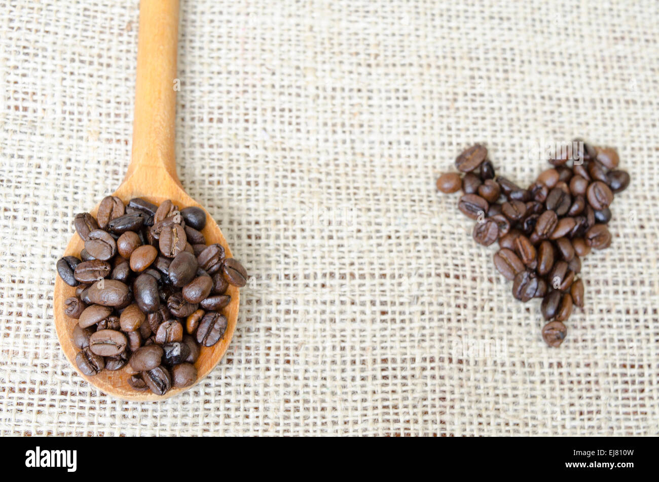 Cucchiaio di legno pieno con chicchi di caffè tostati su una tovaglia vintage Foto Stock