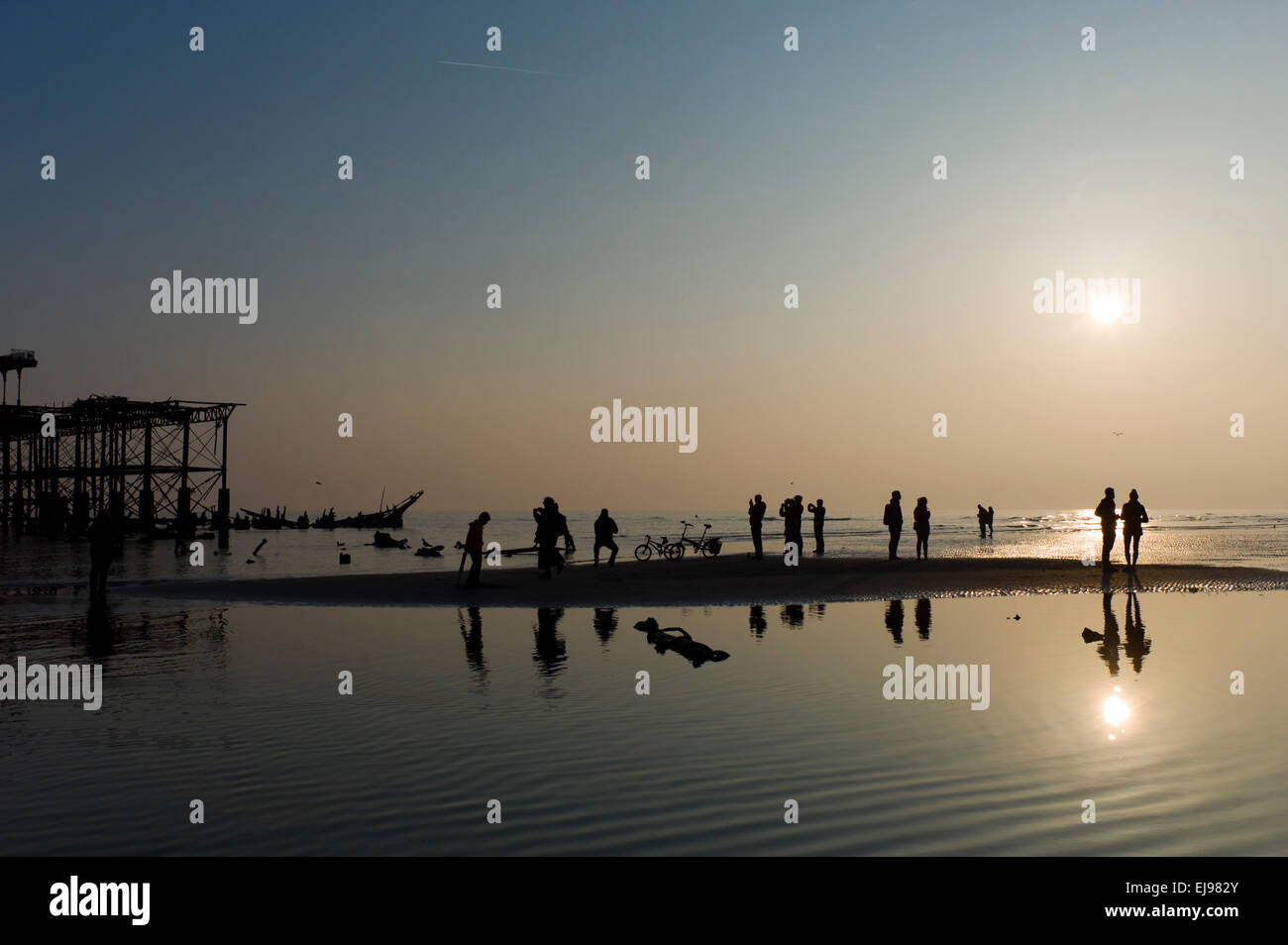 La gente sulla spiaggia e con il minor numero di marea dell'anno, abbandonata Molo Ovest di Brighton,,tramonto, silhouette Foto Stock