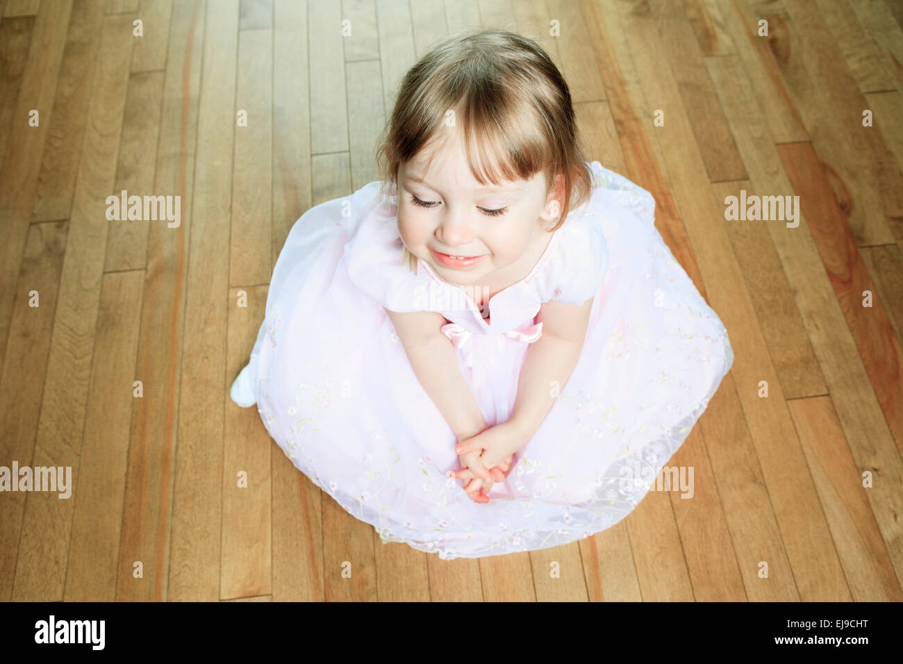 Una bella bambina Siediti sul pavimento con un abito Foto Stock