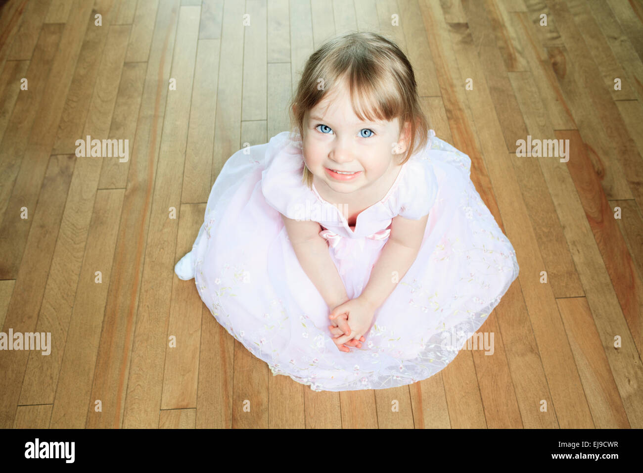 Una bella bambina Siediti sul pavimento con un abito Foto Stock