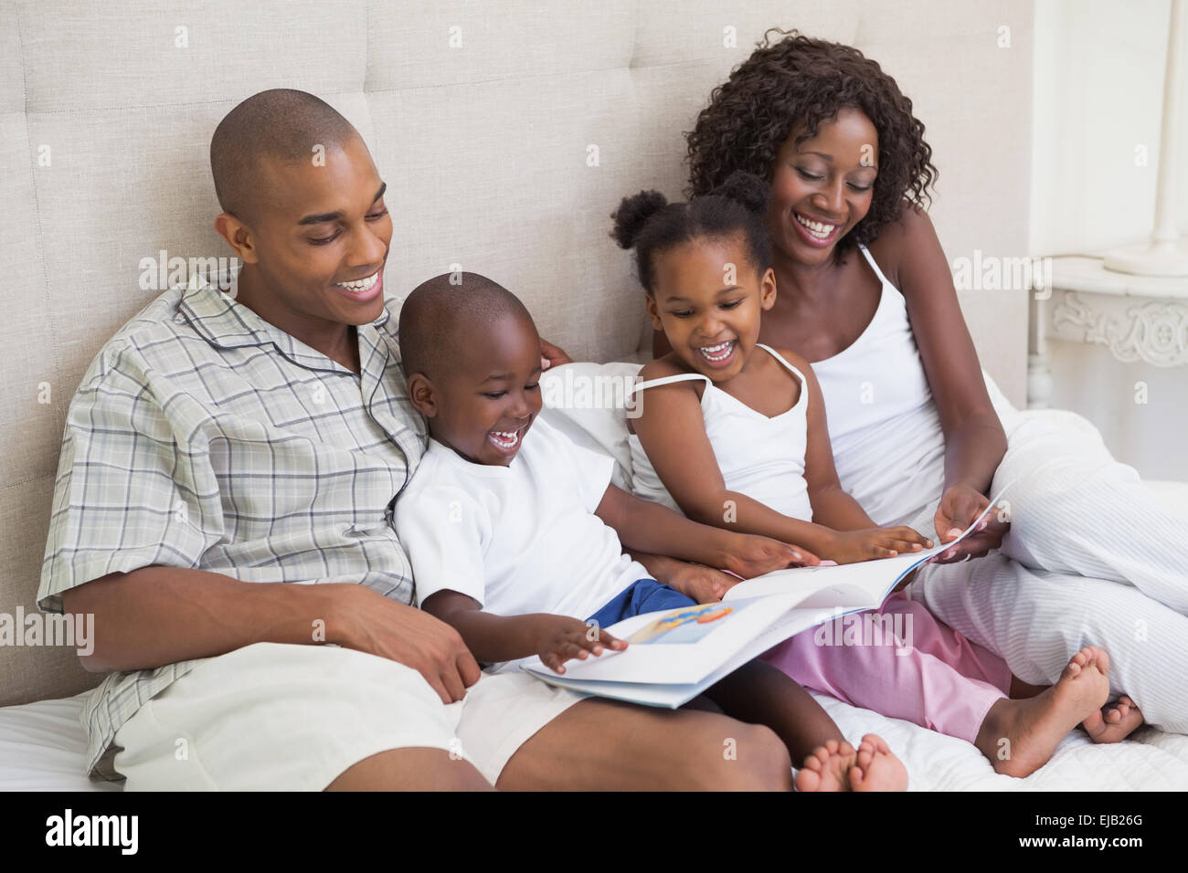 La famiglia felice sdraiato sul letto libro di lettura Foto Stock