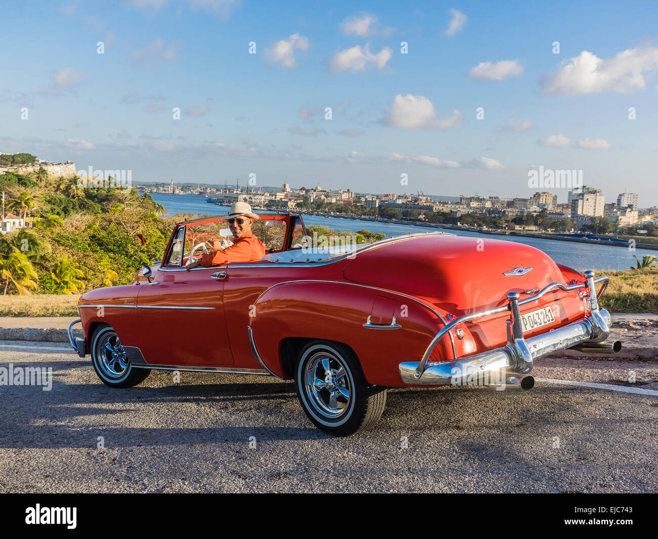 Classic 1950 red Chevy convertibile in Cuba con la parte superiore verso il basso e driver cubano con cappello bianco sulla ruota a. Foto Stock