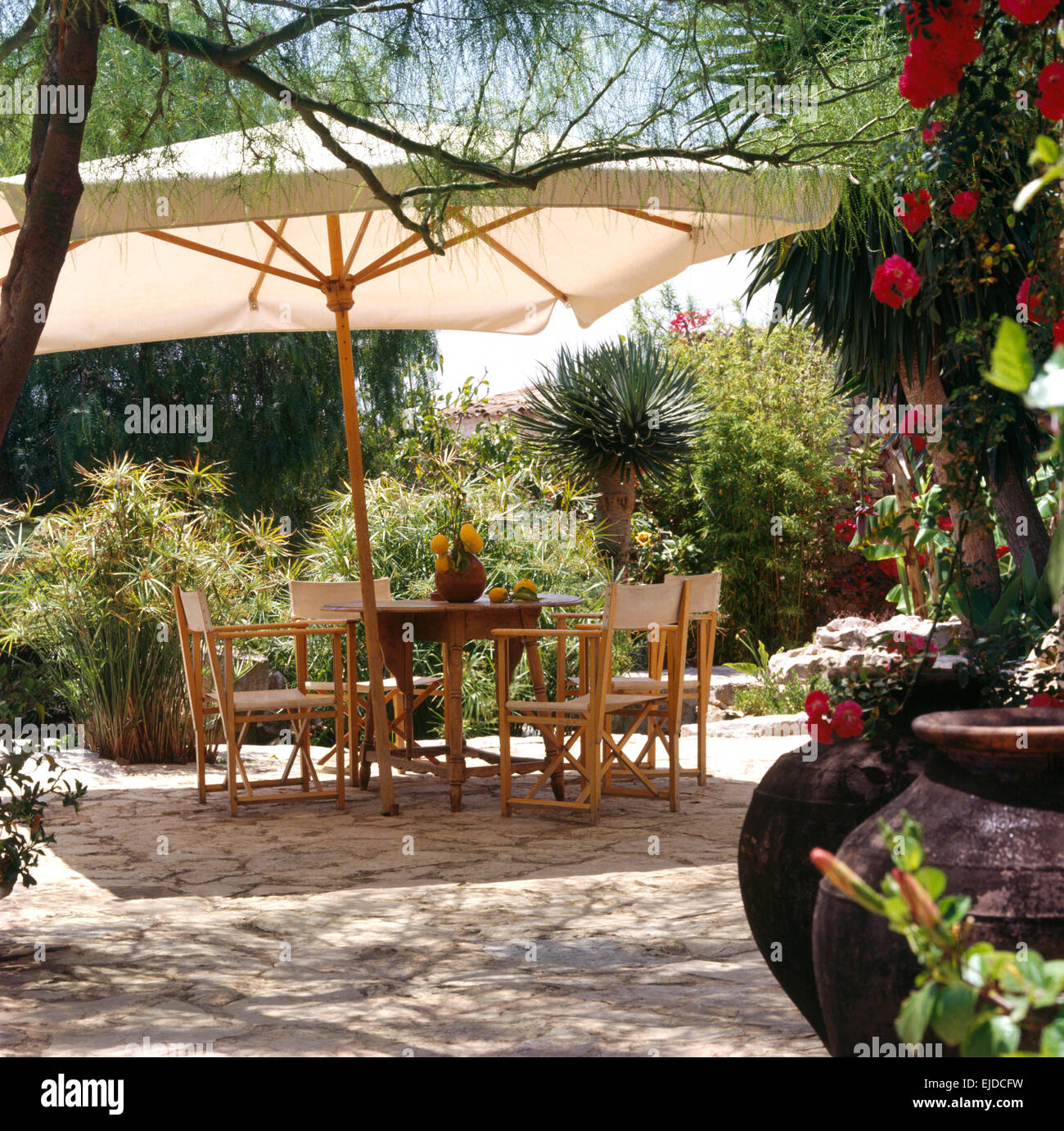 Ombrello bianco al di sopra della tavola e del direttore di sedie sul patio terrazza pavimentata in verde e lussureggiante giardino di Maiorca Foto Stock