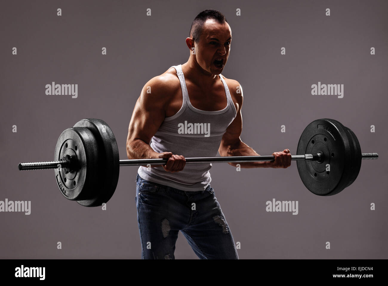 Forte uomo muscolare sollevando una pesante barbell su sfondo grigio scuro Foto Stock