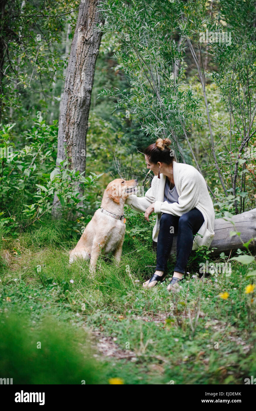 Una donna seduta su un log pacche suo retriever cane. Foto Stock