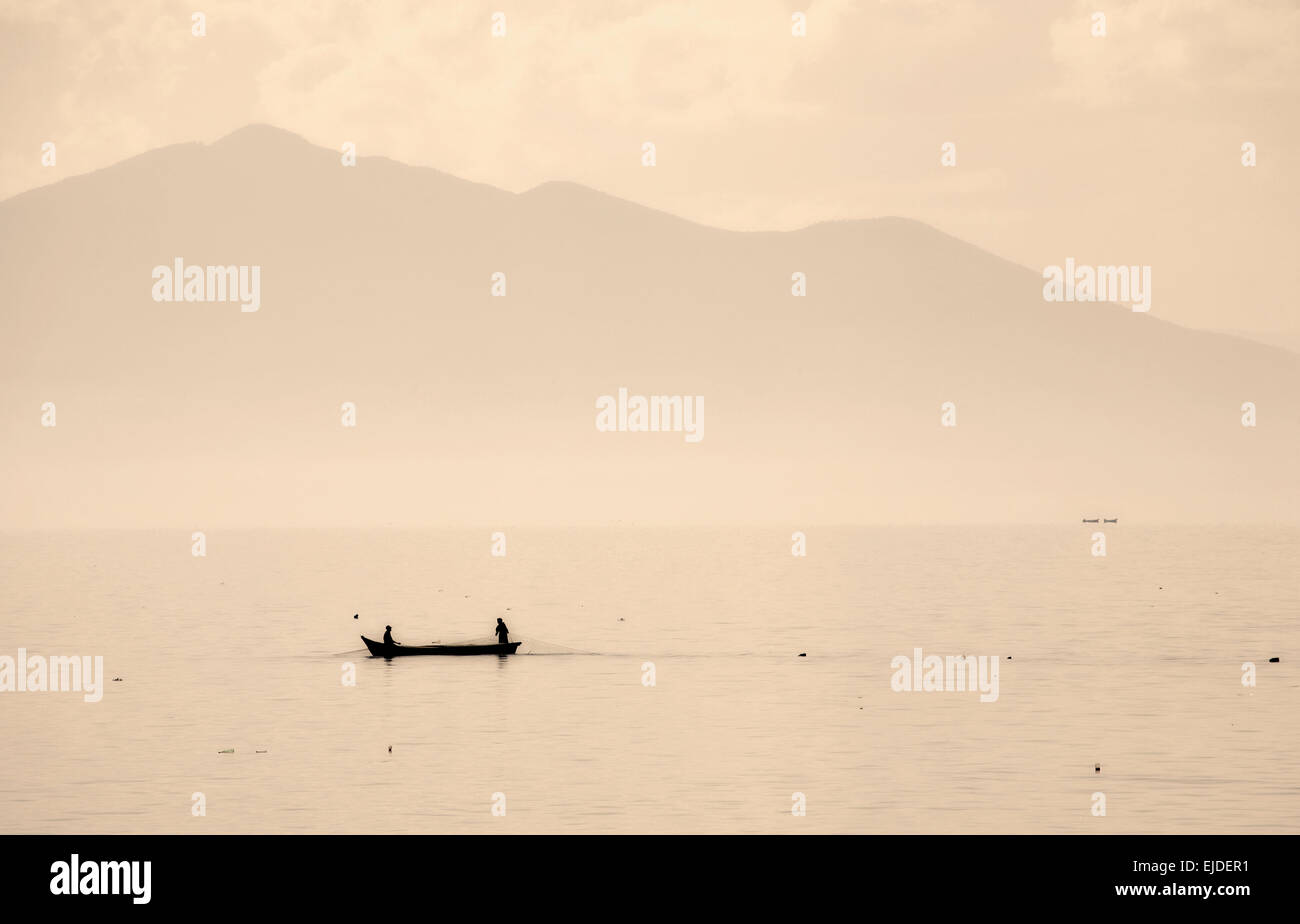 Due persone in una piccola barca da pesca su un lago di disegno nelle reti. Montagne sullo sfondo. Foto Stock