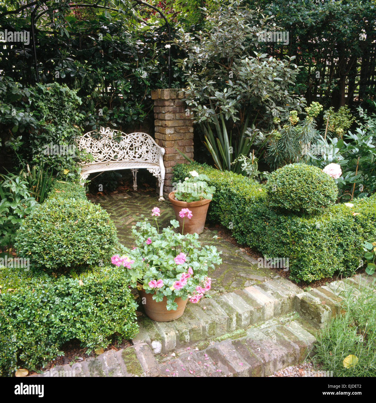 Bassa, ritagliato casella in copertura lastricata di piccole città giardino con un bianco in ferro battuto sul sedile area lastricata Foto Stock