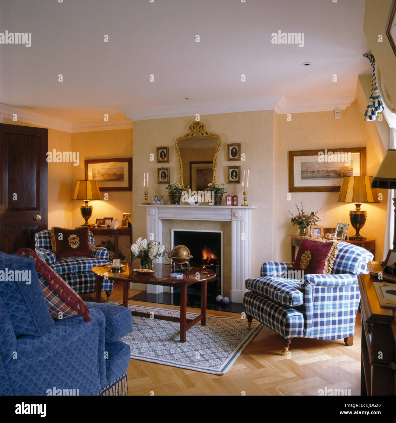 Controllare blu poltrone su entrambi i lati del camino nel tradizionale salotto con lampade illuminate e un divano blu Foto Stock