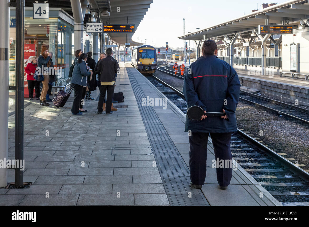 Train Dispatcher e persone in attesa di un treno in arrivo a Derby stazione ferroviaria, England, Regno Unito Foto Stock