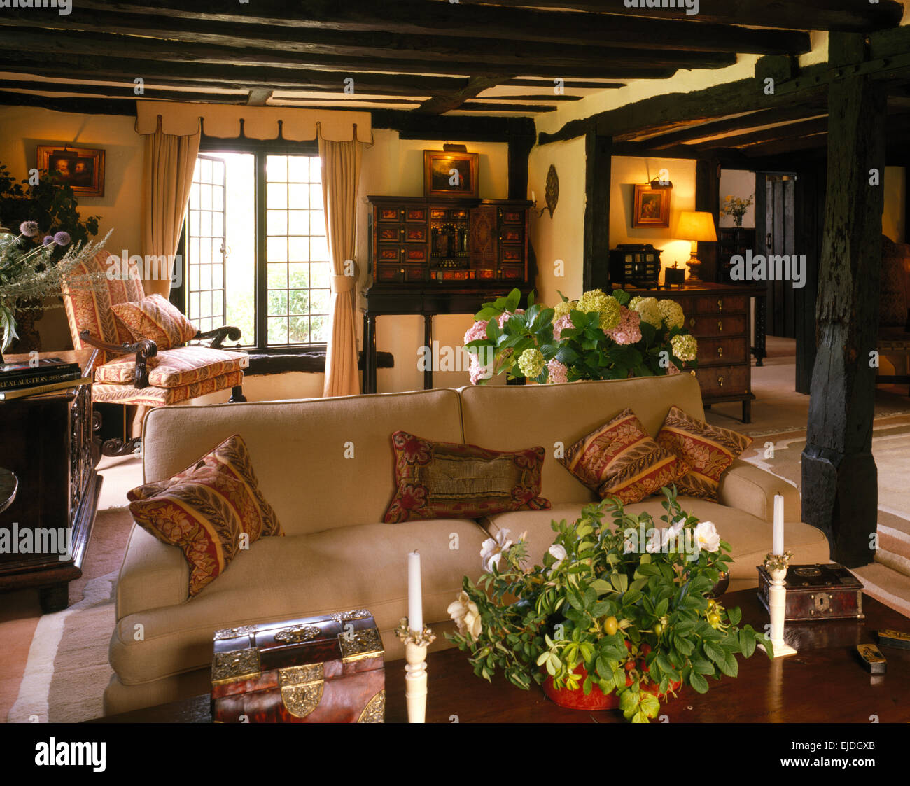 La crema divano nel paese confortevole salotto con soffitto con travi a vista e lampade illuminate Foto Stock